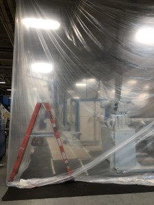 Machine painting area surrounded by plastic sheeting curtain walls hung from the ceiling in a manufacturing facility.