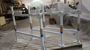 3 rectangle railing metal pieces set on a large pallet in a manufacturing environment taped off in middle and primed in white primer paint.