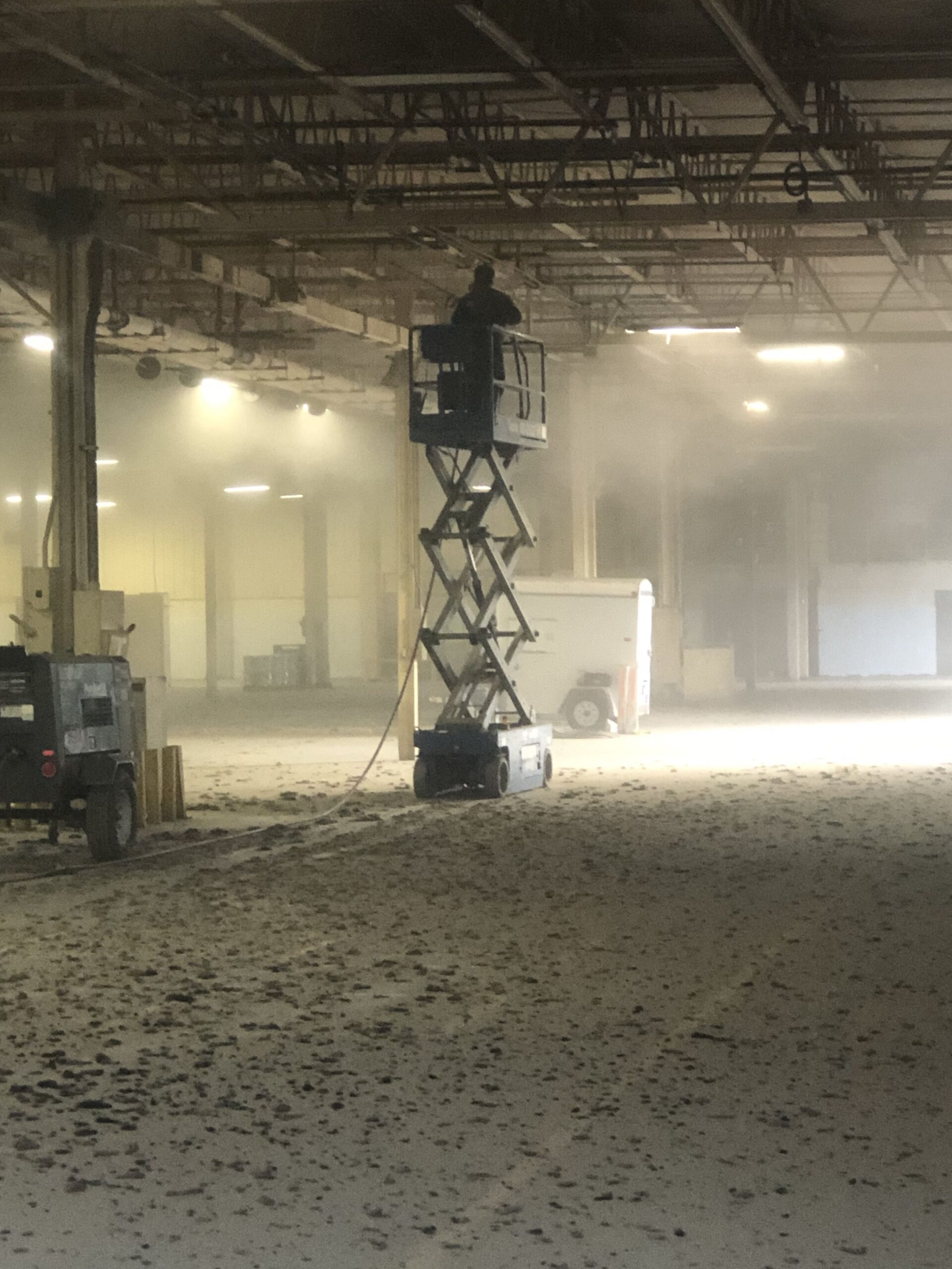 Industrial warehouse ceiling being cleaned by a man on a scissor lift